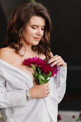 A gentle brunette woman in white clothes with a bouquet of peonies.