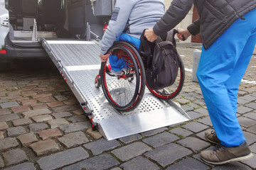 Person on wheelchair with disability using accessible car ramp for transport with help of an...
