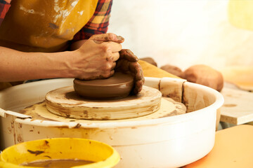 A Potter works with red clay on a Potter's wheel in the workshop.
Women's hands create a pot. Girl sculpts in clay pot closeup. Modeling clay close-up. Warm photo atmosphere. 