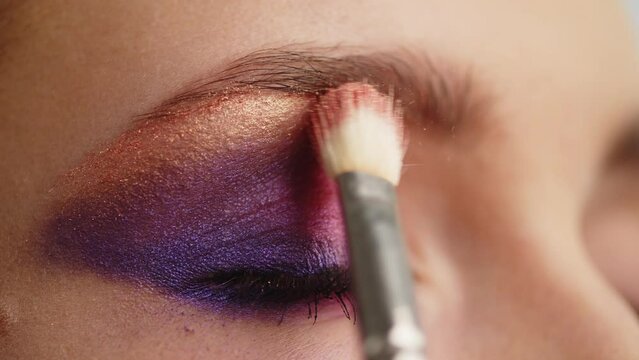 Make-up artist applies makeup to the upper eyelid, close-up.  Makeup artist applies a bright eye shadow with a makeup brush.Tutorial master class of professional makeup. Slow motion cinematic shoot.