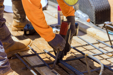 Construction worker hands twisting reinforcement securing steel bars with wire rods for cement reinforcement using rebar tying tool