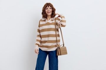 an admiring beautiful woman stands on a white background in a striped sweater smiling happily with her bag pressed to her hip