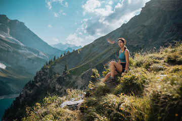 Une femme qui est en montagne lors d'une randonnée et qui regarde le magnifique panorama, avec un lac, des chemins et une forêt.