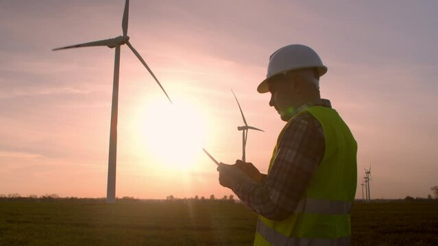 Windmill engineer watching wind turbines in operation on a digital tablet.