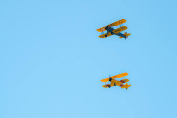 Two biplanes in formation over an airfield during an airshow.