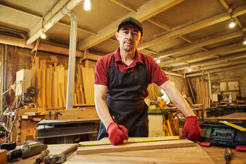 Carpenter working with a wood, marking plank with a pencil and taking measurements to cut a piece of wood to make a piece of furniture in a carpentry workshop