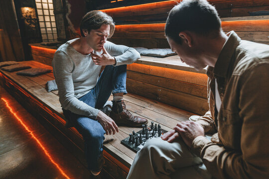 Two friends playing chess sitting on the wooden bench