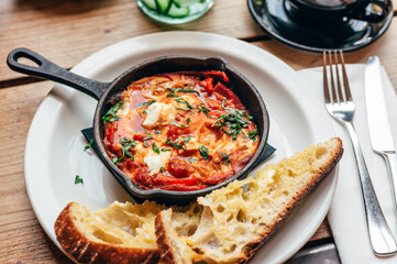 Freshly made shakshuka with spiced tomato, red pepper, feta, egg, coriander and pieces of homemade sourdough, served in iron pan, healthy vegetarian breakfast