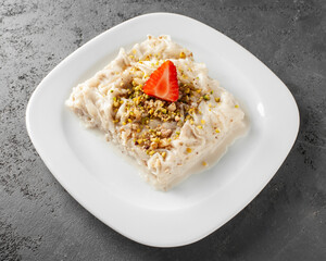 Traditional turkish meal - Gullac. Milk dessert sprinkled with ground nuts and pistachios. Ramadan dish on white plate on grey background
