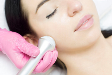 A young woman is lying on the RF-lifting procedure for face skin tightening and face contour correction. Close-up.