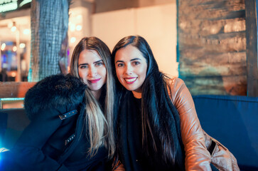 portrait of two beautiful latin women sitting in a pub or restaurant at night