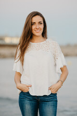 A young woman is posing on a sandy beach near water at twilight in Spain