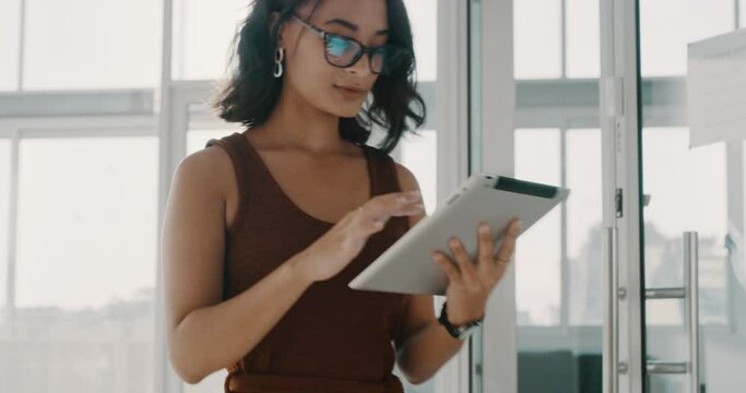 Confident businesswoman using a digital tablet to search and scroll through internet. Serious and focused latino professional updating office schedule. Confident and ambitious designer walking alone