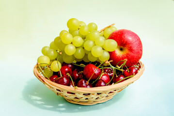 Cherry berries, grapes and a red apple in a wicker plate. Juicy ripe fruits close-up.