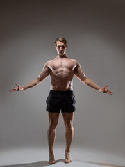 Muscular man in an artistic pose, portrait on a gray background. The guy is an athlete with spectacular muscles posing with his arms outstretched