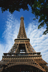 Eiffelturm umrahmt von grünen Bäumen mit blauem Himmel im Hintergrund und Wolken