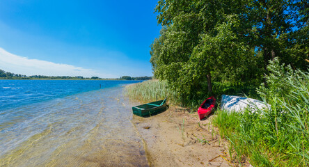 Moored old green fishing boat and red kayak laying on the shallow lakeshore at summertime, both...