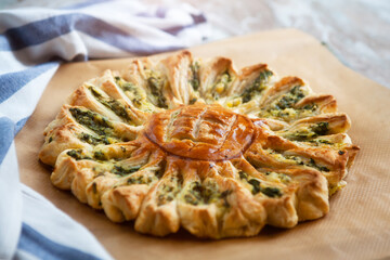 Delicious pie with spinach and ricotta cheese in the shape of a sunflower, towel next to it, close-up.