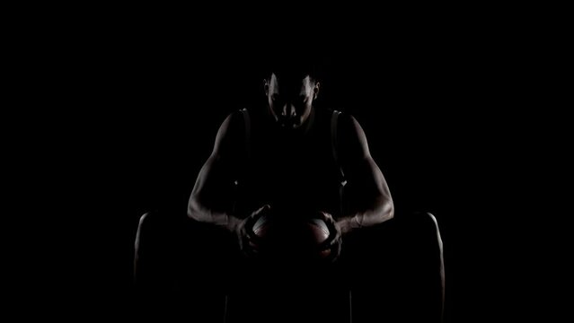 Basketball player sitting on a bench. Concentrated african american sports man against black background.