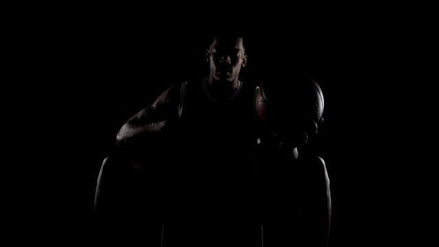Basketball player sitting on a bench praying. Religious african american sports man against black background.