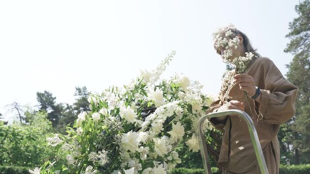 Wedding decor concept. A woman florist makes an arch with flowers for a wedding ceremony. Close-up. Stands on the stairs and works with flowers.