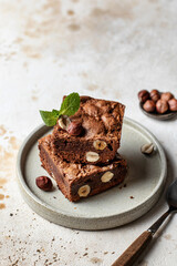 Stack of chocolate brownies with hazelnuts and mint leaf on a plate with spoon with text space
