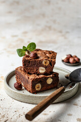 Stack of chocolate brownies with hazelnuts and mint leaf on modern plate with spoon, copy space