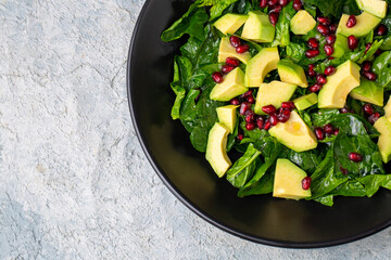 Avocado salad with spinach and pomegranate in a black plate on black background.