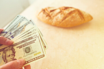 A woman counts money in on the background of a loaf of bread. Finance, family budget, income, poverty, wellbeing concept.