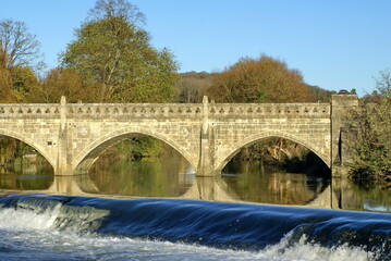 Obraz premium Autumn foliage around a bridge above a dam on the River Avon in Bath, England, UK