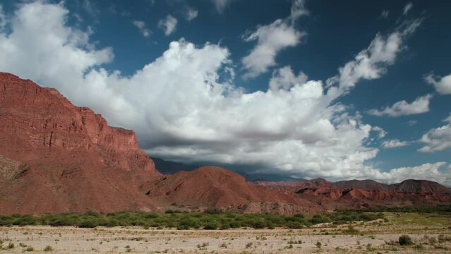Time lapse in the arid desert. View of the red sandstone mountains and white clouds passing by.