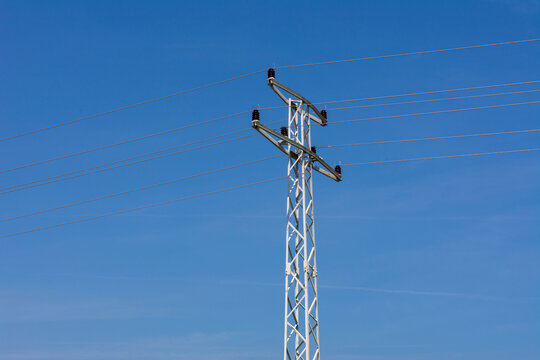 Electric support of high voltage power cables. Metal pole with high voltage wires and glass insulators against clear blue sky.