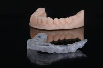 Printed transparent dental cap made of polymer on a light colorful background. Dental splint against bruxism.