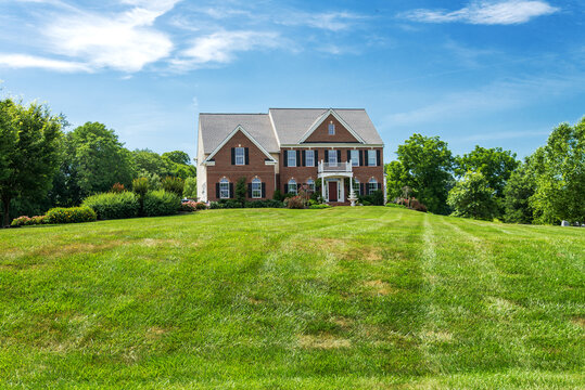 beautiful brick country house in the suburbs of Leesburg, Virginia with trees and a spacious green lawn in the foreground.