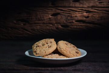 Chocolate chip cookies on linen napkin in white plate on wooden table. Stacked chocolate chip cookies close up.