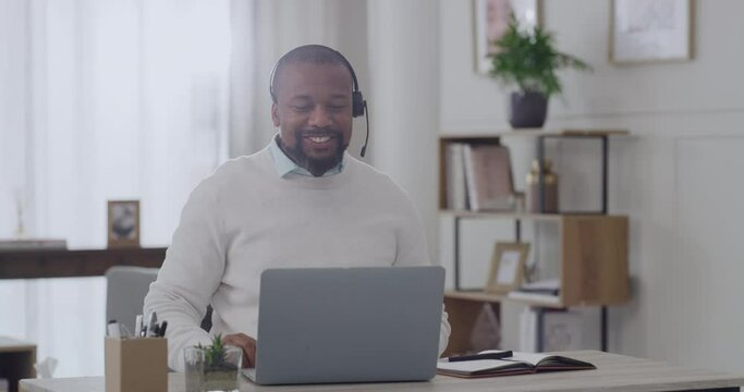 Call centre agent using a headset to listen and talk to clients on a video conference on home office laptop. Confident freelance entrepreneur, customer service operator sitting alone, helping customer