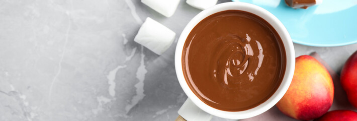 Fondue pot and marshmallow dipped into milk chocolate on light grey table, flat lay with space for text. Banner design