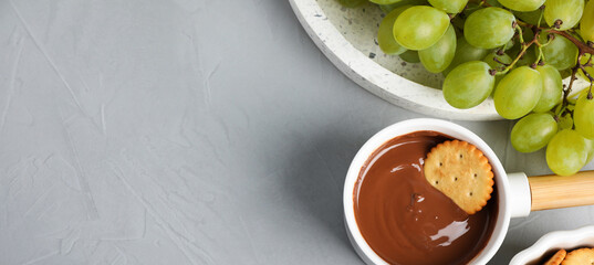 Dipping cookie into pot with chocolate fondue on grey table, flat lay with space for text. Banner...
