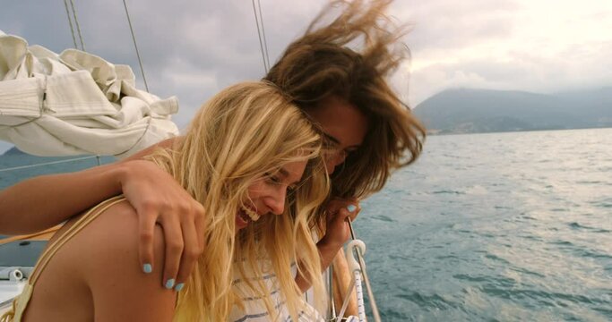 Happy friends hugging and laughing on a cruise on a seaside holiday. Cheerful women relaxing and bonding on a yacht on the ocean. Joyful sisters spending time together on a boat ride on a cloudy day