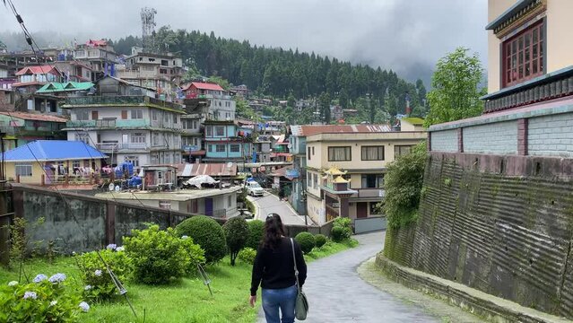 Rear view of Happy young Indian girl walking through mountain roads in Darjeeling with hill top houses and forest in the background.