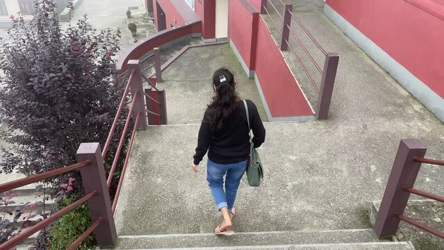 Rear view of Happy young Indian girl in black dress walking through stairs of a monastery.