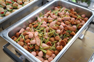 Spicy stir fried with meatballs and morning glory in buffet line. The container is a rectangular stainless steel tray. Selective focus.