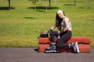 Sporty young woman stretching and resting after skating in a park on a sunny day