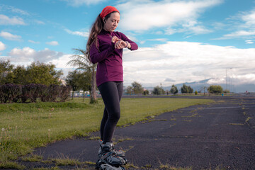 young sporty woman practicing inline skating in an urban setting. Prepare sportwatch and headphones