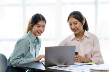 Two young Asian professional businesswomen working talking in a modern startup with laptop computer at the office..