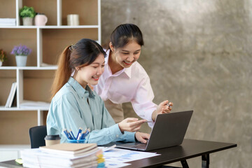 Two young Asian professional businesswomen working talking in a modern startup with laptop computer at the office..