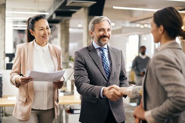 Happy CEO shaking hands with job candidate at corporate office.