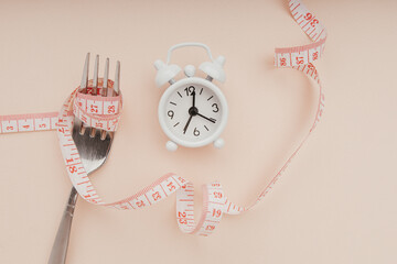 Measure tape roll on fork and alarm clock. Diet, health and fitness concept