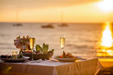 Foto op Plexiglas Romantic sunset dinner on the beach. Table honeymoon set for two with luxurious food, glasses of champagne drinks in a restaurant with sea view. Summer love, romance date on vacation concept. © TravelMedia