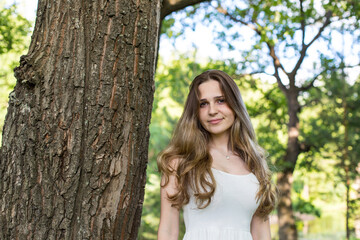 Fototapeta na wymiar Beautiful young Russian girl dressed in a white dress, walks through the forest among the oaks in the rays of the sunset